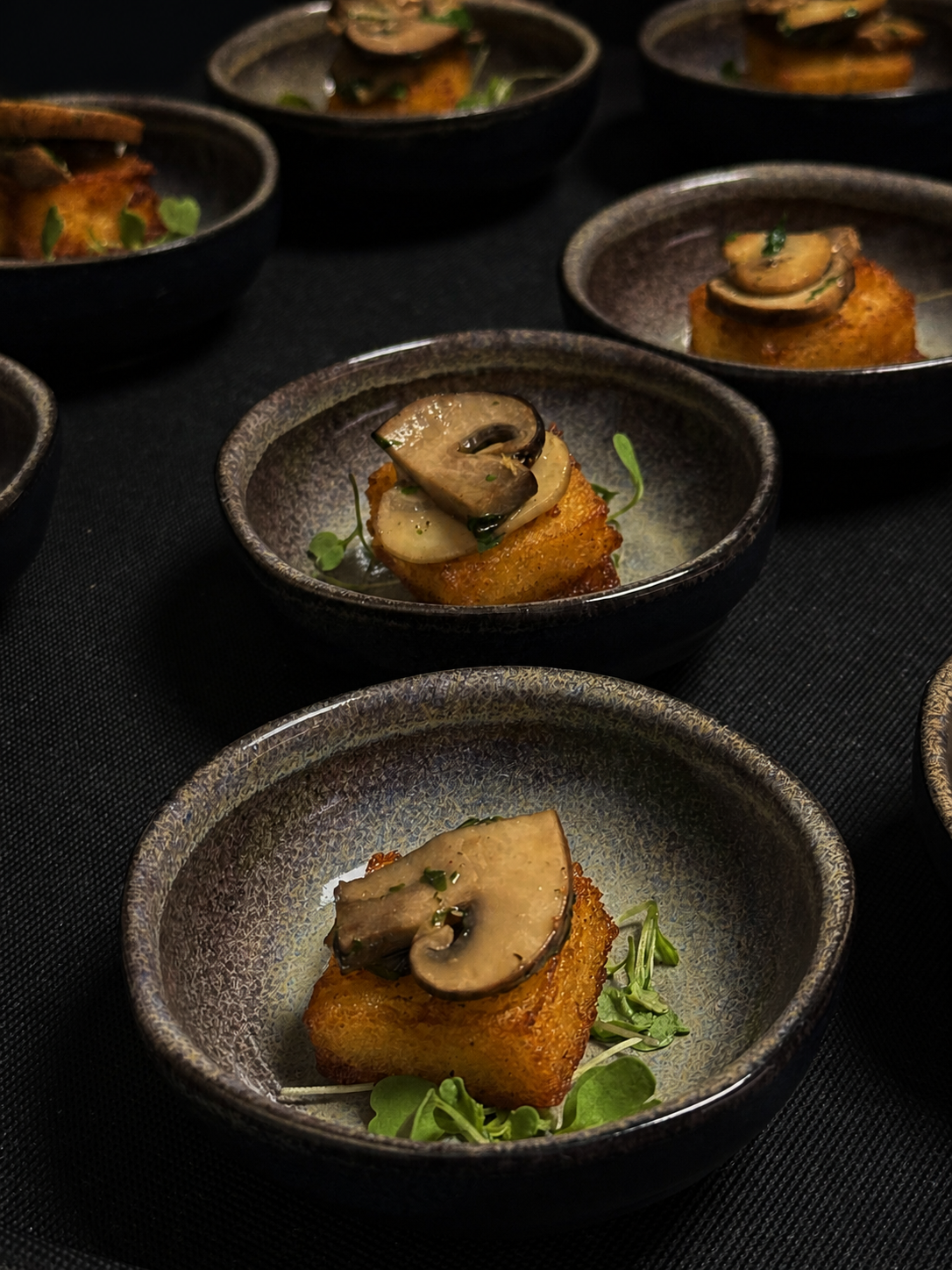 Finger food servido em pequenas louças artesanais durante um evento noturno